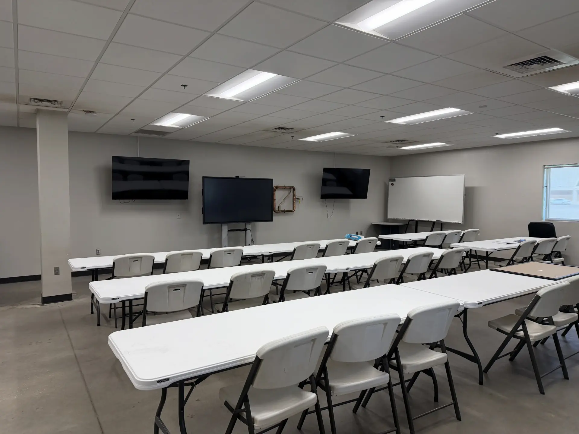 Empty classroom with screens, a whiteboard, and three rows of seats