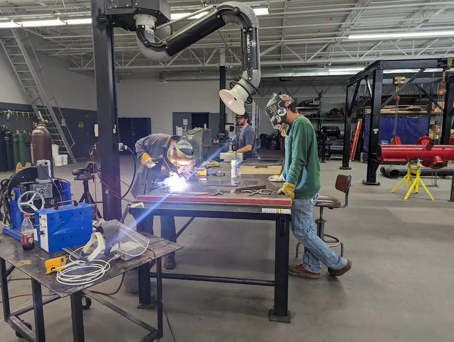 Person welding something with another person watching